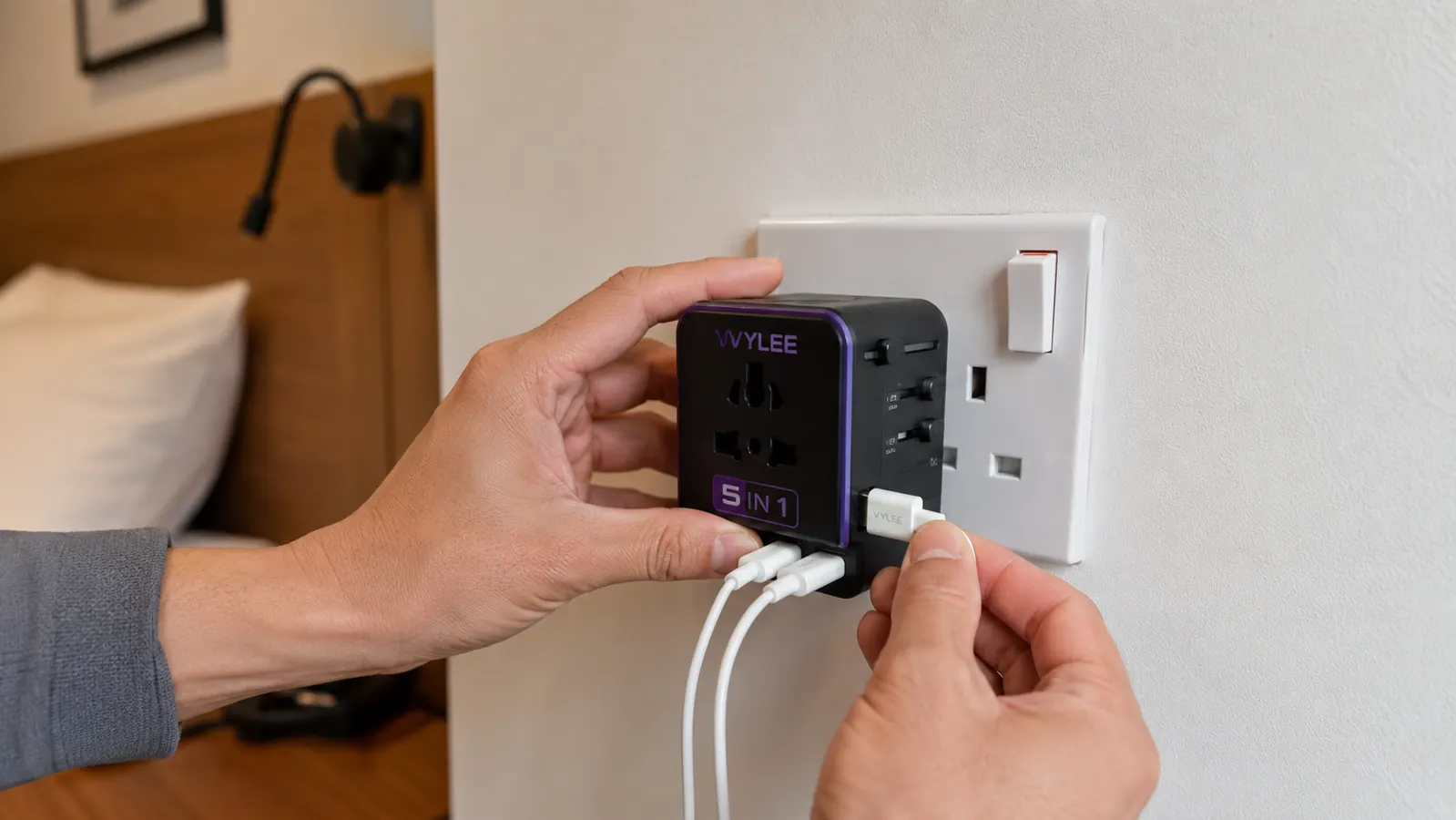 Hand inserting VYLEE universal travel adapter into a UK Type-G wall outlet in a hotel room