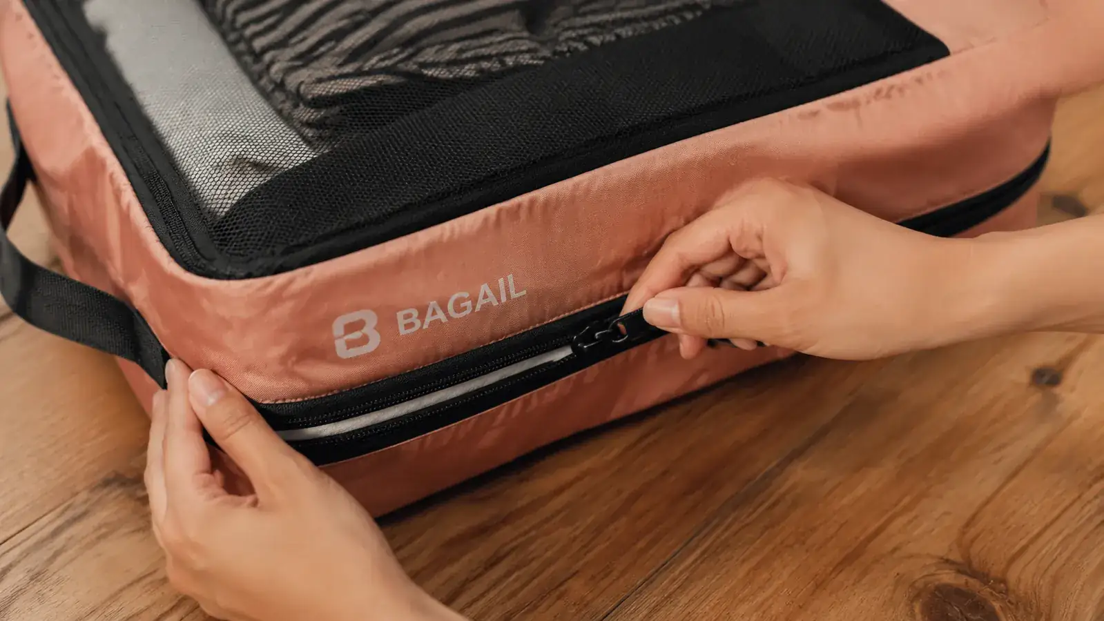 Hands zipping the compression zipper closed on a BAGAIL packing cube stuffed with folded shirts