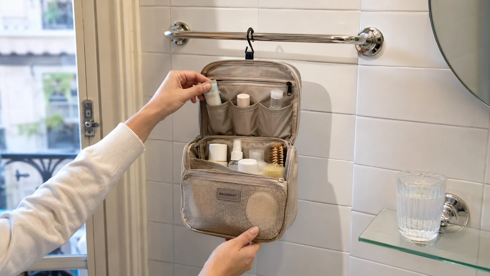 BAGSMART hanging toiletry bag unzipped and hanging from a chrome bathroom hook in a small European hotel bathroom