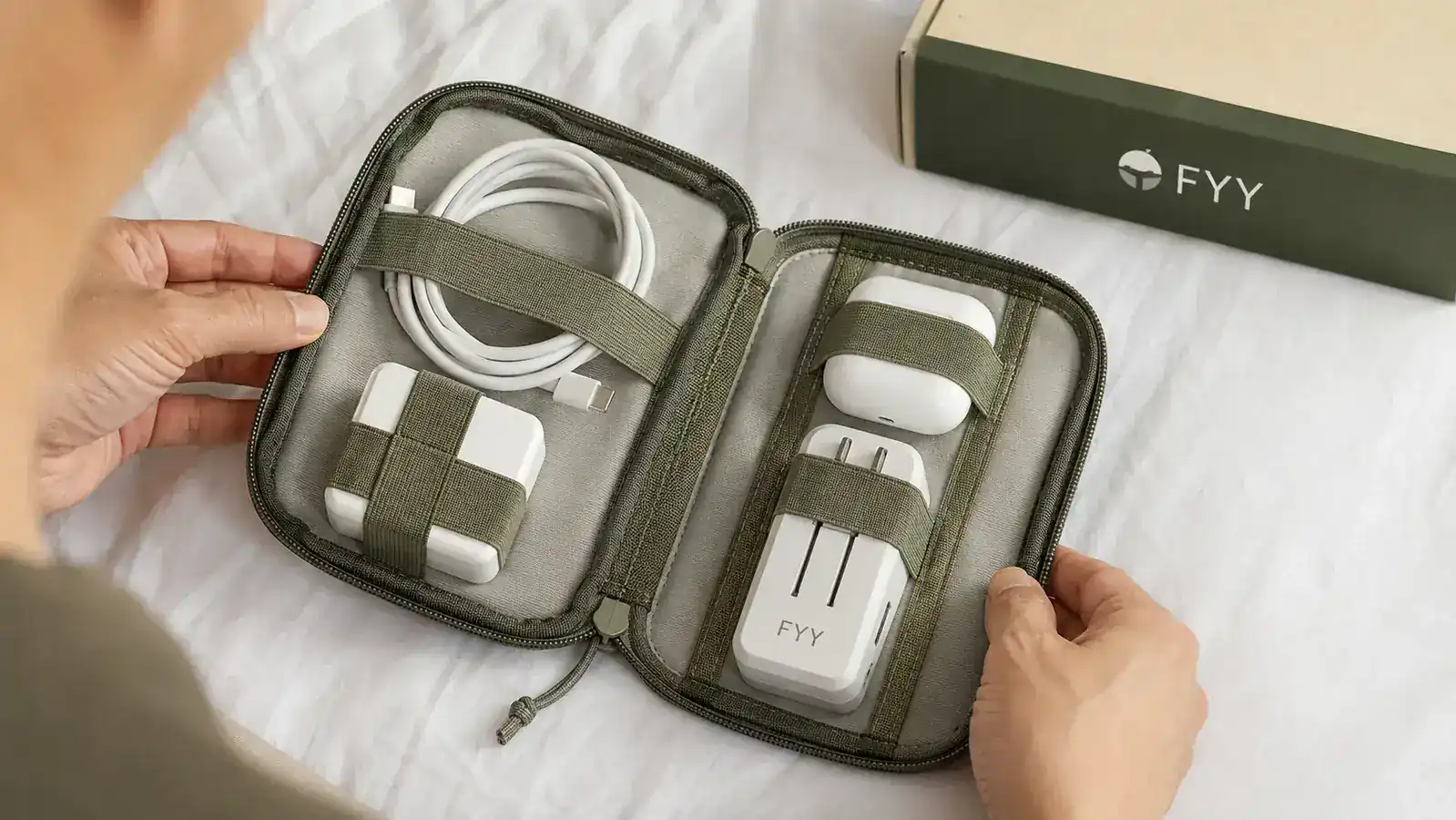 FYY cable organizer pouch lying open on a hostel bed, neatly holding USB cables, earbuds, and a charging brick