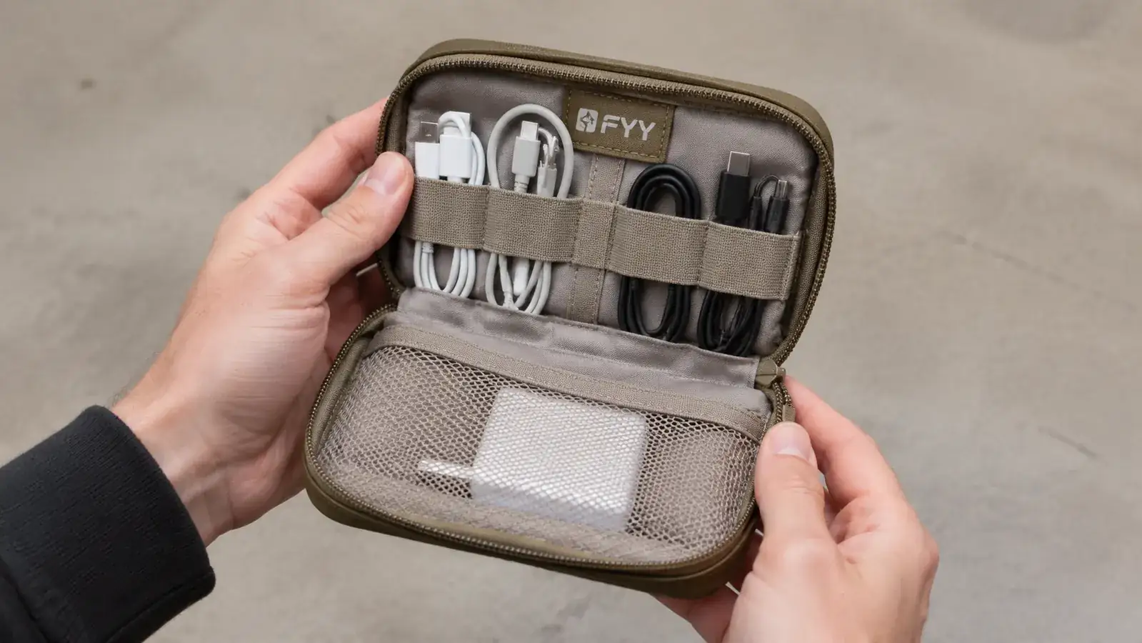 Hand holding the FYY cable organizer pouch open to show interior elastic loops and mesh pockets stuffed with cables and a travel adapter