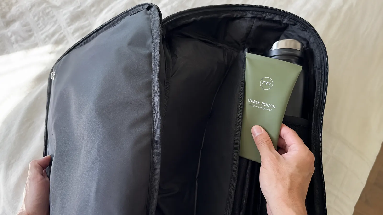 Travel bag interior showing the FYY cable pouch tucked neatly into a slim side pocket alongside a water bottle