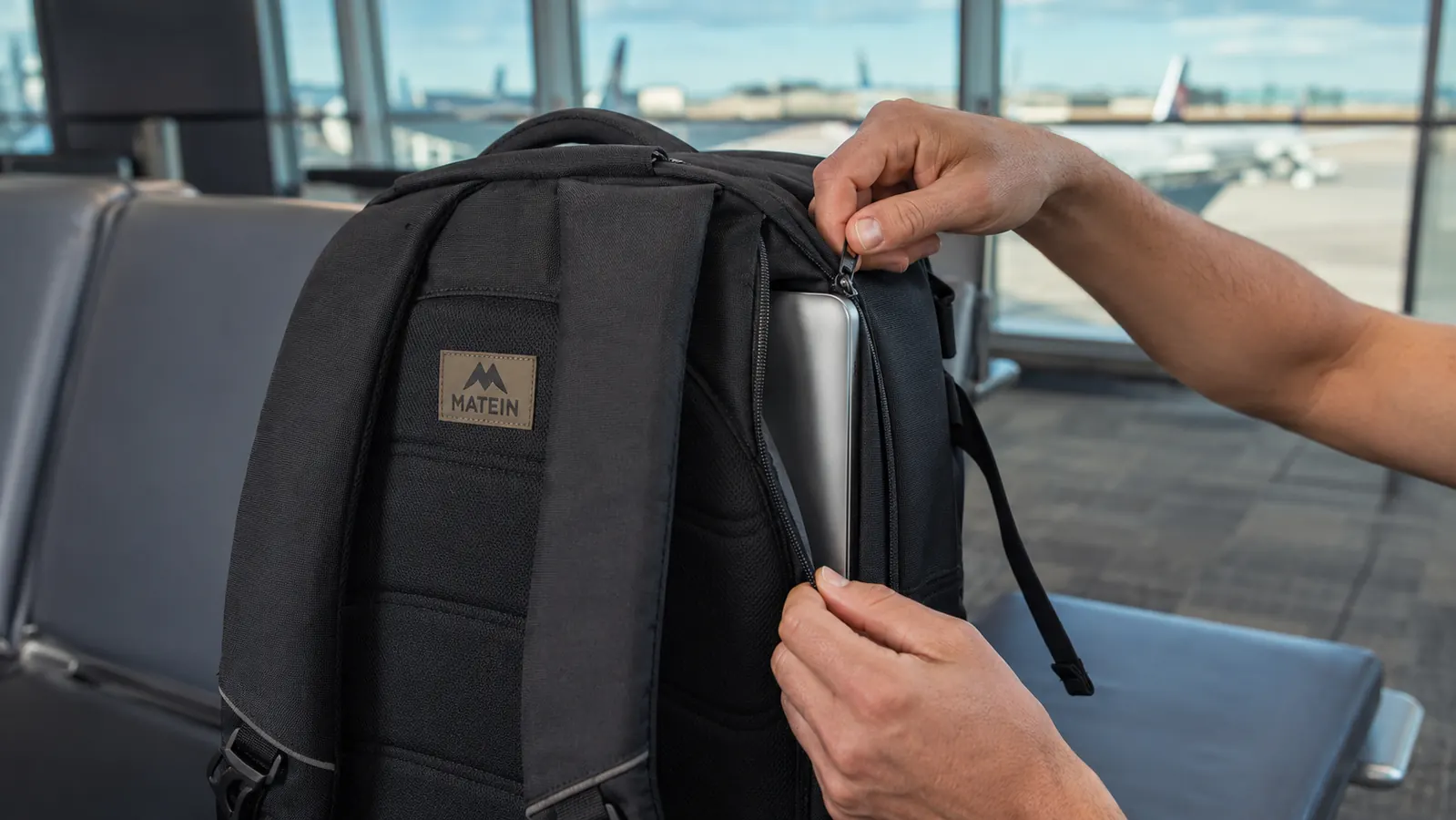 Hand opening the hidden back panel zipper on the MATEIN backpack to access a laptop